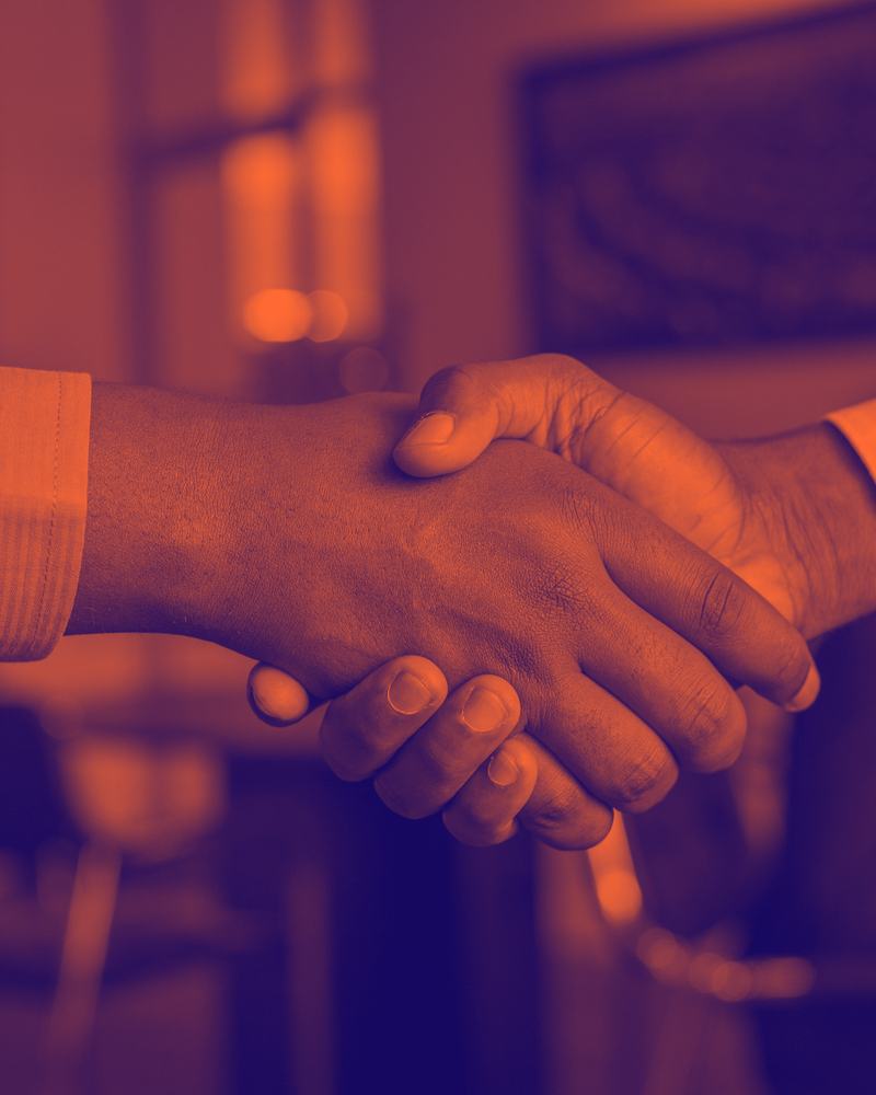 Two professionals shaking hands across a table after a face-to-face meeting